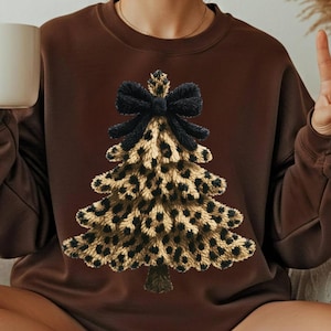 May include: Dark chocolate-colored sweatshirt featuring a leopard print Christmas tree design with a black bow at the top. The tree has a brown trunk. The sweatshirt is a crew neck style.