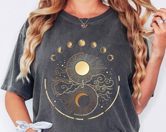 Puede incluir: Una camiseta gris carbón con un gráfico dorado de un diseño yin-yang de sol y luna rodeado por un ciclo de fases lunares. El texto Pepper está impreso en la esquina superior izquierda. La camiseta tiene cuello redondo y mangas cortas.