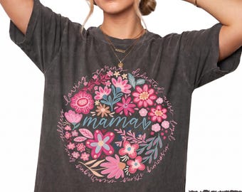 May include: A charcoal grey short-sleeve t-shirt featuring a circular floral graphic in shades of pink, blue, and white. The word mama is printed in the centre in blue script, surrounded by words like loving, caring, dedicated, wise, and loyal.