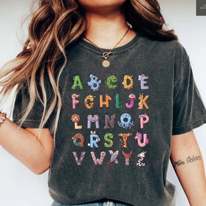 May include: A dark gray t-shirt with a colorful alphabet printed on the front. Each letter is formed by a different animal or insect. The text "Mon Océan" is visible on the right arm.