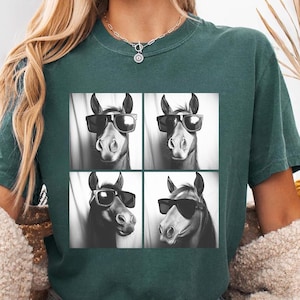 May include: A teal green t-shirt with a black and white image of four horses wearing sunglasses. Each horse has a different expression.