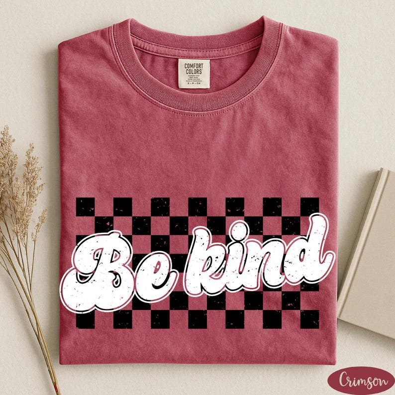 Pu&ograve; includere: Una t-shirt a maniche corte color cremisi con un motivo a scacchi nero e cremisi al centro. Il testo bianco "Be kind" &egrave; stampato sopra il motivo a scacchi in un carattere grassetto e arrotondato con una texture usurata e invecchiata.