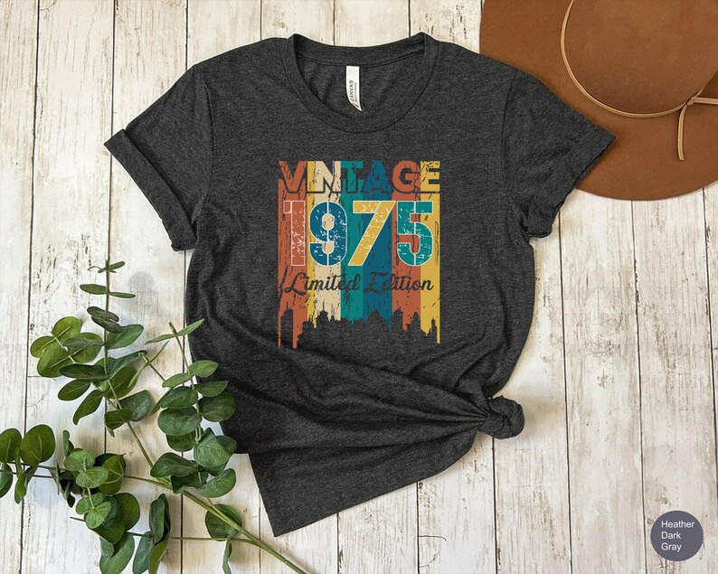 May include: Dark heather gray t-shirt with a vintage design. The graphic features the text "VINTAGE 1975 Limited Edition" in a colorful, distressed style. The shirt is knotted at the bottom and has a tag at the neckline.