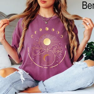 Pu&ograve; includere: T-shirt color bacca con un design celeste dorato raffigurante un sole, una luna e le fasi lunari. La maglietta ha una vestibilit&agrave; ampia e maniche corte. La parola "Berry" &egrave; stampata in alto a destra.