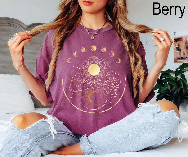 Pu&ograve; includere: T-shirt color bacca con un design celeste dorato raffigurante un sole, una luna e le fasi lunari. La maglietta ha una vestibilit&agrave; ampia e maniche corte. La parola "Berry" &egrave; stampata in alto a destra.