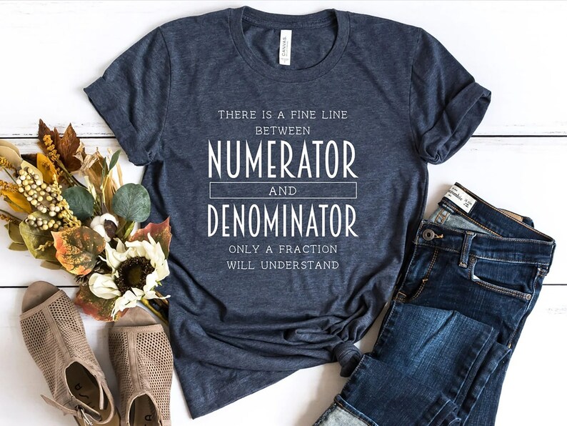 May include: Dark blue t-shirt with white text: "THERE IS A FINE LINE BETWEEN NUMERATOR AND DENOMINATOR ONLY A FRACTION WILL UNDERSTAND." The shirt is styled with blue jeans and beige open-toe shoes. The shirt is made of a soft material.
