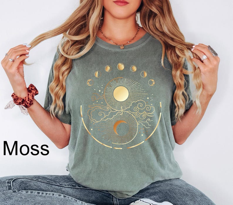 Pu&ograve; includere: Una maglietta verde muschio con un design celeste dorato raffigurante un sole, le fasi lunari e nuvole. La parola "Moss" &egrave; stampata in nero in basso a sinistra. La maglietta ha maniche corte e girocollo.