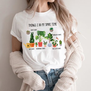 May include: White t-shirt with the text "THINGS I DO MY SPARE TIME" and illustrations of plants. The graphic includes the phrases "REPOT PLANTS", "PROPAGATE PLANTS", "BUY PLANTS", "REARRANGE PLANTS", and "TALK WITH PLANTS".
