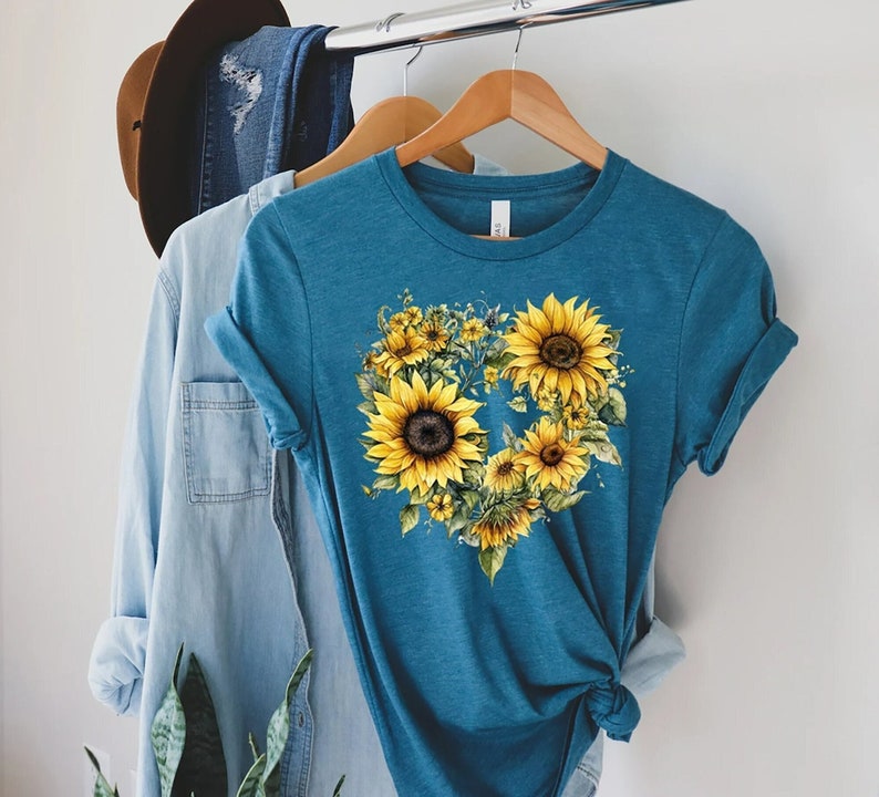 May include: A teal blue t-shirt with a heart-shaped design featuring yellow sunflowers and green leaves.