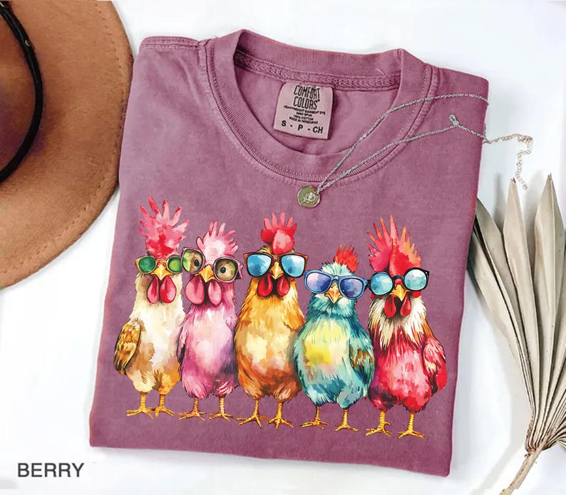 Puede incluir: Una camiseta morada con un gr&aacute;fico de cinco pollos con gafas de sol. Los pollos est&aacute;n dibujados en un estilo de dibujos animados con plumas y picos coloridos. El texto "Comfort Colors" est&aacute; impreso en la camiseta.