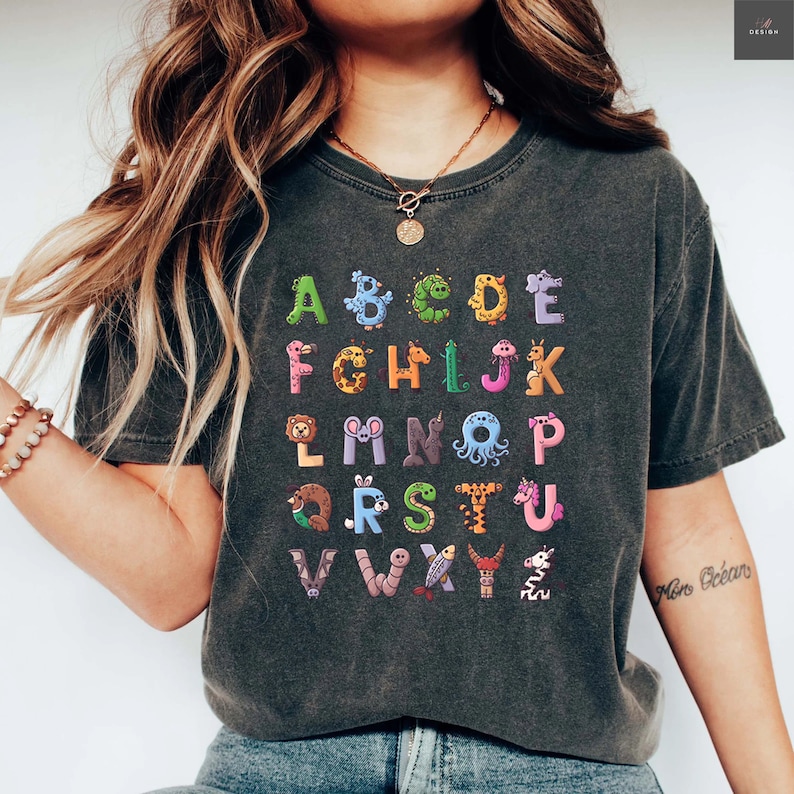 May include: A dark gray t-shirt with a colorful alphabet printed on the front. Each letter is formed by a different animal or insect. The text "Mon Océan" is visible on the right arm.