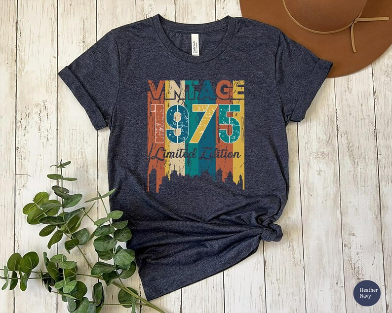 May include: Heather navy blue t-shirt with a vintage design. The design features the word "VINTAGE" above the number "1975" and the words "Limited Edition" in a retro color scheme of orange, yellow, teal, and brown.