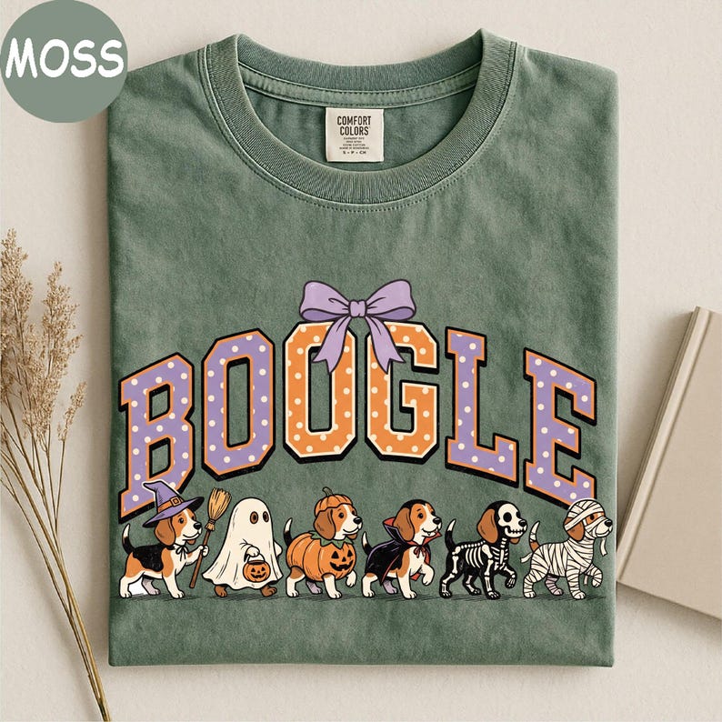 K&ouml;nnte beinhalten: Ein moosgr&uuml;nes T-Shirt mit dem Schriftzug BOOGLE in orangefarbenen und violetten gepunkteten Buchstaben und einer violetten Schleife dar&uuml;ber. Darunter sind sechs Beagle-Hunde in Halloween-Kost&uuml;men abgebildet: Hexe, Geist, K&uuml;rbis, Vampir, Skelett und Mumie.