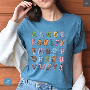 May include: Teal t-shirt featuring a colorful alphabet design. Each letter is creatively illustrated with an animal or creature, creating a fun and educational visual. The shirt is made of a soft material.