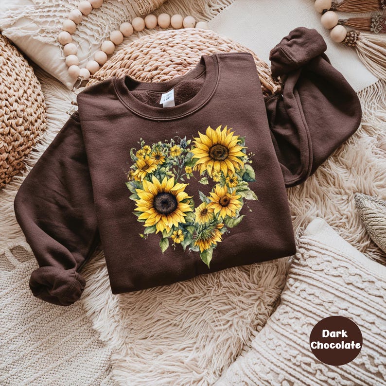 Pode incluir: Um moletom marrom escuro com um design de girassol em forma de cora&ccedil;&atilde;o. O design inclui girass&oacute;is amarelos com folhas verdes. O texto "Dark Chocolate" est&aacute; em um c&iacute;rculo. O moletom est&aacute; em uma superf&iacute;cie texturizada.