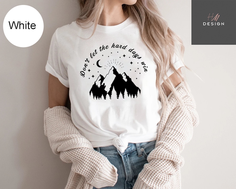 Pu&ograve; includere: T-shirt bianca con grafica di montagna nera, luna crescente, stelle e la scritta "Don't let the hard days win." La maglietta &egrave; realizzata in materiale morbido ed &egrave; adatta per l'abbigliamento casual.