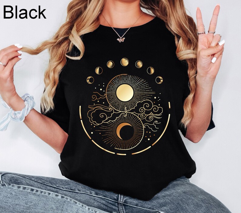 Pu&ograve; includere: T-shirt nera con un disegno dorato di sole e luna con fasi lunari. La maglietta ha un girocollo e maniche corte. La parola "Black" &egrave; stampata in alto a sinistra.