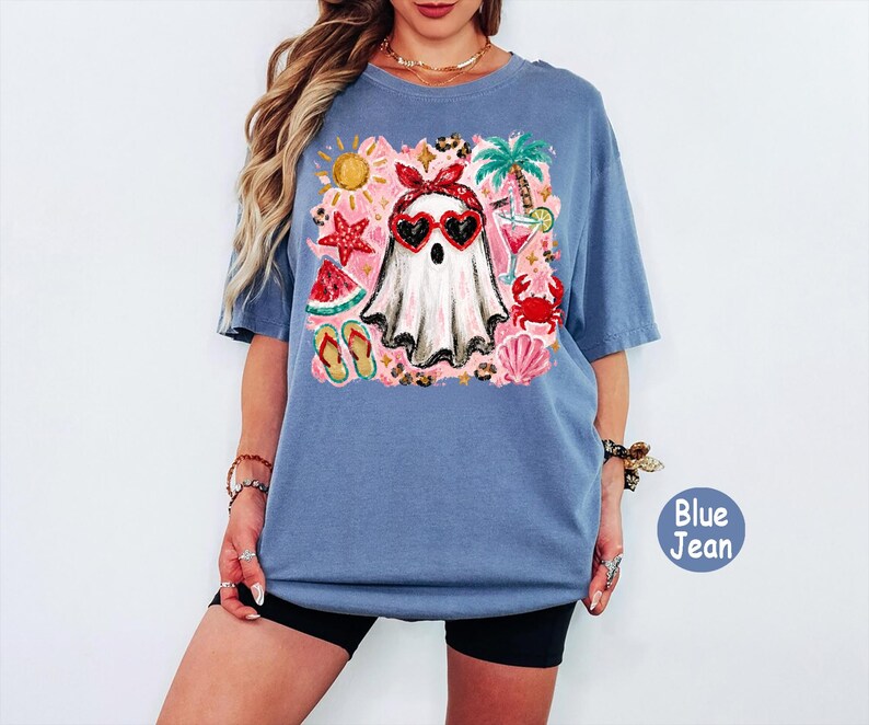 May include: A blue jean colored t-shirt featuring a central graphic of a white ghost wearing a red bandana and heart-shaped sunglasses. The design includes summer icons like a palm tree, starfish, watermelon slice, flip-flops, and a cocktail.