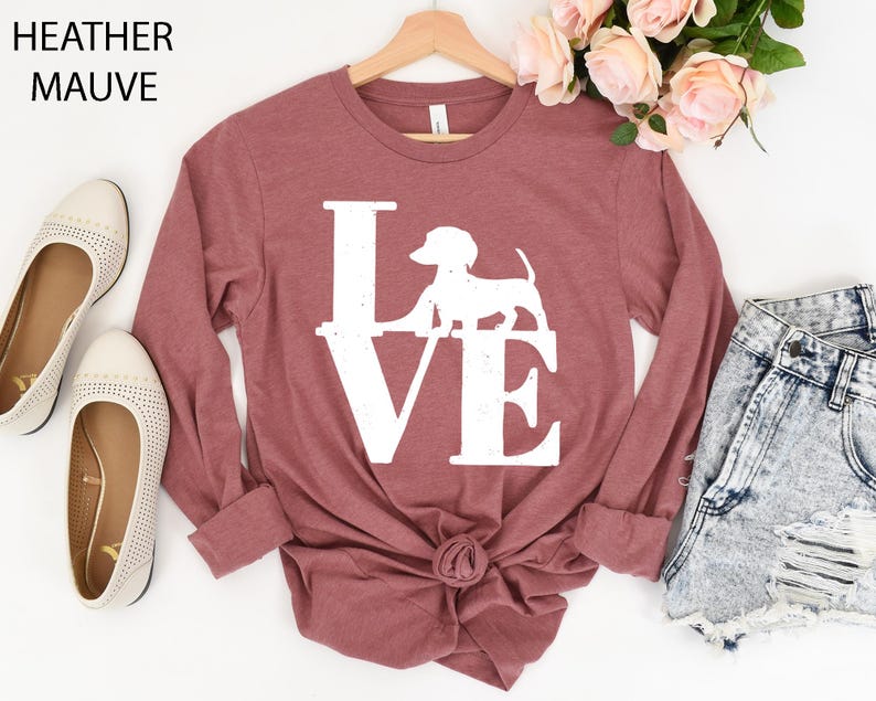 May include: Heather mauve long-sleeve shirt with a white "LOVE" graphic featuring a dachshund silhouette. The shirt is styled with a knot at the waist and is displayed with denim shorts and flats. The text "Heather Mauve" is at the top.