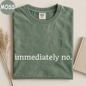 May include: A moss green short-sleeved t-shirt with a crew neckline and a garment-dyed finish. The center of the chest features the white text "immediately no." in a serif font. The interior neck label reads "Comfort Colors" with size S P CH.