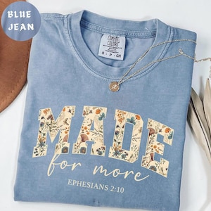 May include: Blue jean Comfort Colors t-shirt with the words "MADE for more" in a floral design. The text "Ephesians 2:10" is printed below. A gold necklace with a pendant is on the shirt.