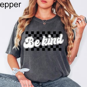 Pu&ograve; includere: Una t-shirt a maniche corte grigio antracite con una grafica rettangolare a scacchi bianchi e neri e la scritta Be kind in un carattere bianco in stile retr&ograve;. La maglietta presenta un girocollo e una texture del tessuto slavata.