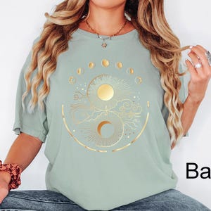 Pu&ograve; includere: T-shirt verde salvia con un design celeste dorato raffigurante sole, luna e fasi lunari. La grafica &egrave; centrata sul davanti. La maglietta ha maniche corte e una vestibilit&agrave; ampia.