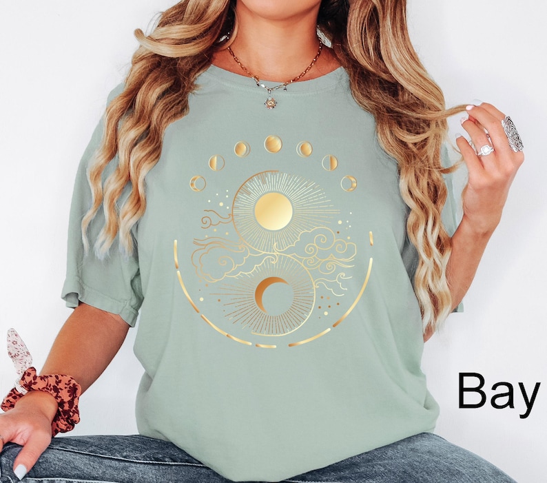 Pu&ograve; includere: T-shirt verde salvia con un design celeste dorato raffigurante sole, luna e fasi lunari. La grafica &egrave; centrata sul davanti. La maglietta ha maniche corte e una vestibilit&agrave; ampia.