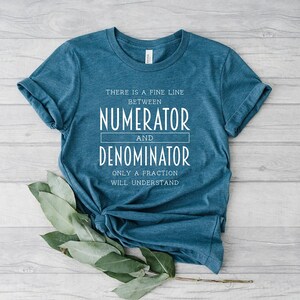 May include: Teal-colored t-shirt with the text "THERE IS A FINE LINE BETWEEN NUMERATOR AND DENOMINATOR ONLY A FRACTION WILL UNDERSTAND" in white. The shirt is styled with rolled-up sleeves and a knot at the bottom.