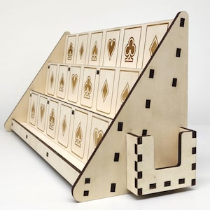 Könnte beinhalten: Ein Spielkartenhalter aus Holz mit drei Reihen Spielkarten. Die Karten sind in einer gestaffelten Anordnung angeordnet, wobei jede Karte ein Kartensymbol aufweist. Der Halter ist aus hellem Holz gefertigt und hat einen Schlitz für zusätzliche Karten.