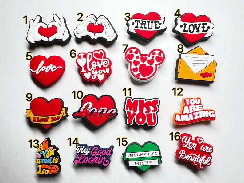 May include: A set of 16 colorful shoe charms featuring hearts, love-themed messages, and other designs. The charms are made of rubber and have a variety of colors, including red, white, yellow, green, and pink.