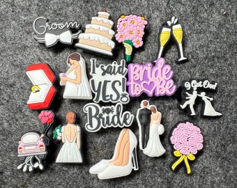 May include: A collection of wedding-themed charms in various shapes and colors. Includes a cake, bouquet, high heels, a car, and text that says "Groom", "I said YES!", "Bride to be", and "Got One!"