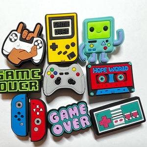 May include: A set of nine colorful game-themed charms, including a retro game console, a cassette tape, a controller, and a Nintendo Switch. The charms feature the words "Game Over" in various styles.