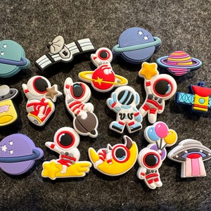 May include: A collection of 15 colorful space-themed shoe charms, including astronauts, planets, spaceships, and stars.