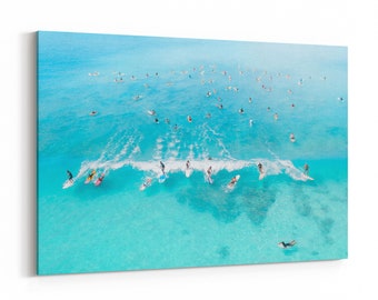 May include: An aerial view of a group of people surfing in a turquoise ocean. The surfers are riding waves and paddling in the water. The water is clear and blue, and the sky is bright.