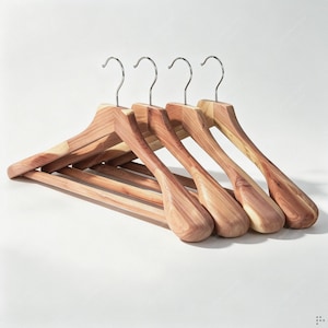 Op de afbeelding: Een set van vier houten kledinghangers met een natuurlijke roodbruine houtnerfafwerking. Elke hanger heeft een glad, voorgevormd schouderontwerp en een zilverkleurige metalen draaibare haak aan de bovenkant om kledingstukken veilig op te hangen.