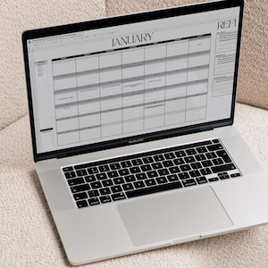 A MacBook sits on a boucle armchair with the 2023 Marketing Calendar Template  visible on the laptop screen.