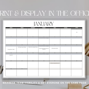 A mock up of the January month calendar hanging on a wall is showed infront of a background of a desk in an office setting with pencils in a caddy and a gold lamp. Text reads: Print & Display In The Office, Maximise team visibility