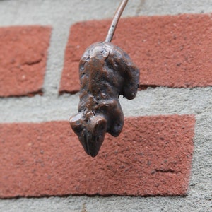May include: A small, brown, metal sculpture of a mouse hanging from a brick wall.