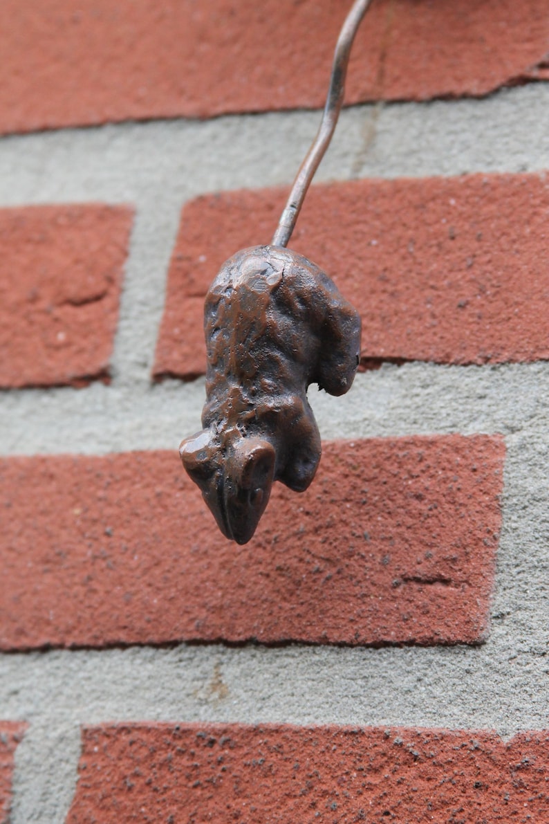 May include: A small, brown, metal sculpture of a mouse hanging from a brick wall.