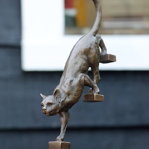 a bronze sculpture of a cat walking down the stairs
