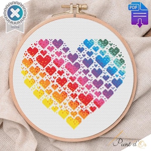 May include: A cross stitch pattern of a rainbow heart made up of smaller hearts. The pattern is in a wooden embroidery hoop.