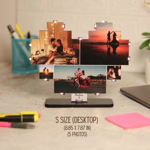May include: A heart-shaped photo frame with five photos of a couple. The frame is made of wood and has a black base. The frame is lit up with small white lights. The frame is 8.85 inches wide and 7.87 inches tall. The text "Pauline & Daniel" is written on the base of the frame.