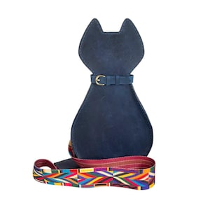 May include: A blue leather cat-shaped bag with a colourful woven strap. The bag has a gold buckle and a flap that closes with a snap.
