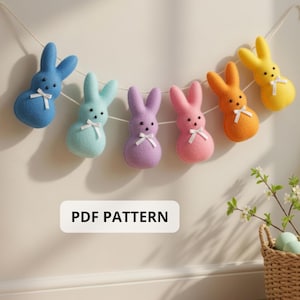 Könnte beinhalten: Eine farbenfrohe Osterhasen-Girlande mit sechs Filzhasen in Blau, Hellblau, Lila, Rosa, Orange und Gelb. Jeder Hase hat eine weiße Schleife und schwarze Perlenaugen. Die Girlande ist an einer weißen Schnur aufgereiht. Der Text "PDF PATTERN" ist sichtbar.