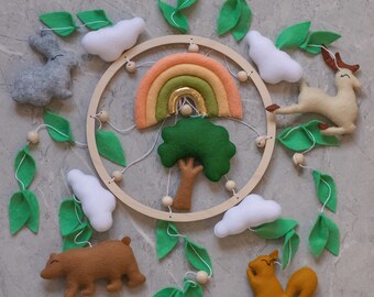 May include: A wooden mobile with felt woodland animals, clouds, and leaves. The animals include a deer, a bear, a squirrel, and a rabbit. The mobile also features a rainbow and a green tree.