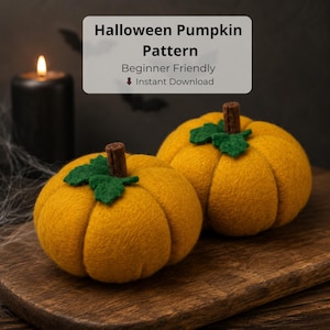 Op de afbeelding: Twee gele viltpompoenen met groene vilten bladeren en bruine steeltjes. De tekst luidt: Halloween Pumpkin Pattern, Beginner Friendly, Instant Download. Een zwarte kaars en spinnenwebben zijn zichtbaar op de achtergrond van de afbeelding.
