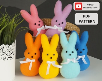 May include: Five felt Easter bunny plush toys in different colors: pink, orange, yellow, blue, and light blue. Each bunny has a white ribbon tied around its neck and black button eyes. The bunnies are arranged in a semi-circle on a white surface. The text "VIDEO INSTRUCTION" and "PDF PATTERN" is visible in the image.
