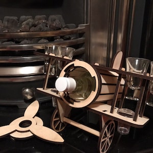 Könnte beinhalten: Holz-Flaschenhalter in Flugzeugform mit einer Weinflasche im Inneren und vier Schnapsgläsern. Der Halter hat Räder und einen Propeller.