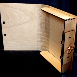 Può includere: Una scatola di legno con un coperchio incernierato e un buco della serratura decorativo. La scatola è realizzata in legno chiaro e ha una finitura naturale.